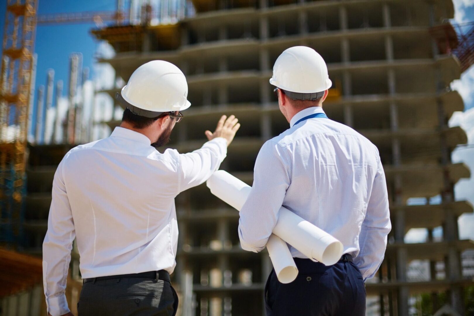 Two men in white hard hats standing next to a building.